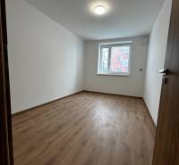 3-izbový byt v štandarde vrátane kuchyne len 15 minút od BA - Prázdna izba v 4-izbovom byte s podlahou s dreveným dekorom a bielymi stenami.