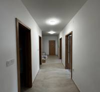 3-izbový byt v štandarde vrátane kuchyne len 15 minút od BA - Chodba v 4-izbovom byte s dlažbou a drevenými zárubňami, osvetlená stropnými svietidlami.