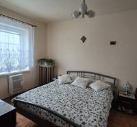 3 IZBOVÝ RODINNÝ DOM S GARÁŽOU, VEĽKÉ OZOROVCE - Spálňa v rodinnom dome so vzorovaným prehozom, televíziou a podlahou s dreveným dekorom.