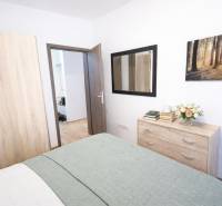 REZERVOVANÉ Prenájom  2-izbového bytu v Petržalke - Spálňa v 2-izbovom byte so skriňou, komodou a podlahou s dreveným dekorom.