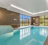 Nadštandardná 6-izbová vila v prominentnej lokalite - Vnútorný bazén vo vile s veľkými oknami, drevenými lavicami a zeleným výhľadom.