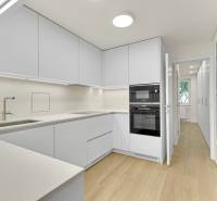 I Na predaj zrekonštruovaný 4i byt v Ružinove, Miletičova - Kuchyňa v 4-izbovom byte s bielou linkou a podlahou s dreveným dekorom.