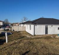 I NA PREDAJ 4i rodinný dom s veľkým pozemkom v Galante - Rodinný dom v Galante s nedokončenou fasádou, okolitým terénom a autami na ulici.