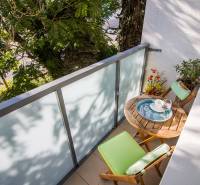 Pozrite si PRÍJEMNÝ 2i byt so ZARIADENÍM, LODŽIOU a KLIMATIZÁCIOU - Balkón 2-izbového bytu s dreveným stolom a stoličkami na ulici Mierová, Bratislava.