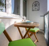 Pozrite si PRÍJEMNÝ 2i byt so ZARIADENÍM, LODŽIOU a KLIMATIZÁCIOU - Balkón v 2-izbovom byte s dreveným stolom, stoličkami a dekoračnou kovovou mriežkou.