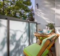 Pozrite si PRÍJEMNÝ 2i byt so ZARIADENÍM, LODŽIOU a KLIMATIZÁCIOU - Balkón 2-izbového bytu s dreveným nábytkom, zelenými vankúšmi a výhľadom na zeleň.