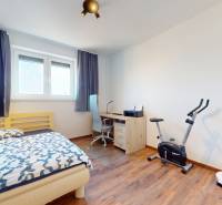 | Exkluzívny 4-izbový byt s obrovskou terasou | Stupava - Izba v 4-izbovom byte s posteľou, pracovným stolom, rotopedom a podlahou s dreveným dekorom.