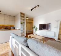 | Exkluzívny 4-izbový byt s obrovskou terasou | Stupava - Obývačka so svetlou pohovkou, kuchyňou a podlahou s dreveným dekorom v 4-izbovom byte.