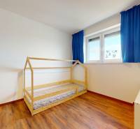 | Exkluzívny 4-izbový byt s obrovskou terasou | Stupava - Detská izba v 4-izbovom byte s podlahou s dreveným dekorom a modrými závesmi.