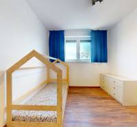 | Exkluzívny 4-izbový byt s obrovskou terasou | Stupava - Detská izba v 4-izbovom byte s podlahou s dreveným dekorom a modrými závesmi.