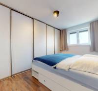 | Exkluzívny 4-izbový byt s obrovskou terasou | Stupava - Spálňa v 4-izbovom byte s posteľou, vstavanou skriňou a podlahou s dreveným dekorom.