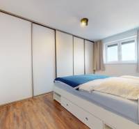 | Exkluzívny 4-izbový byt s obrovskou terasou | Stupava - Spálňa s posteľou, skriňou a podlahou s dreveným dekorom v 4-izbovom byte.