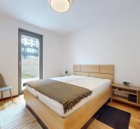 METROPOLIS I Nový Luxusný 2i byt s predzáhradkou I - Spálňa 2-izbového bytu s podlahou s dreveným dekorom, posteľou a stoličkou.