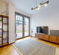 METROPOLIS I Nový Luxusný 2i byt s predzáhradkou I - Obývacia izba v 2-izbovom byte s podlahou s dreveným dekorom, TV a policami.