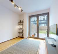 METROPOLIS I Nový Luxusný 2i byt s predzáhradkou I - Izba v 2-izbovom byte s podlahou s dreveným dekorom, televízorom a prístupom na terasu.