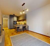 METROPOLIS I Nový Luxusný 2i byt s predzáhradkou I - Obývacia izba s podlahou s dreveným dekorom, kuchynským ostrovom a televízorom v 2-izbovom byte.