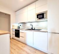 Pekný a moderný 3-izbový byt I Arboria Trnava - Kuchyňa v 3-izbovom byte s bielymi skrinkami a podlahou s dreveným dekorom.