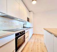 Pekný a moderný 3-izbový byt I Arboria Trnava - Kuchyňa v 3-izbovom byte s podlahou s dreveným dekorom, bielymi skrinkami a vstavanými spotrebičmi.