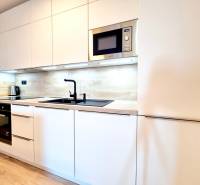 Pekný a moderný 3-izbový byt I Arboria Trnava - Kuchyňa v 3-izbovom byte s bielymi skrinkami a podlahou s dreveným dekorom.