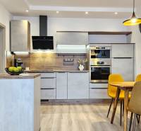 Moderný unikát - 1,5- izb. byt s 2 loggiami na prenájom (Nad jazerom) - Kuchyňa v 1-izbovom byte s podlahou s dreveným dekorom, jedálenský stôl a žlté stoličky.