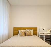 Moderný unikát - 1,5- izb. byt s 2 loggiami na prenájom (Nad jazerom) - Spálňa v 1-izbovom byte so svetlou posteľou, záclonami a bielym stolom s lampou.