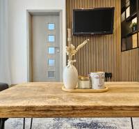 Moderný unikát - 1,5- izb. byt s 2 loggiami na prenájom (Nad jazerom) - Obývacia časť 1-izbového bytu s dreveným stolom a dekoráciami na pozadí s televízorom.