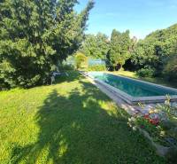 Ponúkame na predaj záhradný domček - Jasová - Záhrada rodinného domu v Jasovej s bazénom obklopená zeleňou a stoličkami.