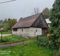 ČREMOŠNÉ-chalupa na pozemku 700m2   - Rustikálna budova na vidieckom pozemku, obklopená stromami a trávou, blízko rodinného domu.