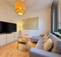 2-izbový byt 45m2 | Sklenárová - Ružinov - Obývačka v 2-izbovom byte s podlahou s dreveným dekorom, sedačkou a TV.