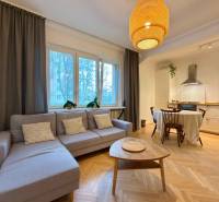 2-izbový byt 45m2 | Sklenárová - Ružinov - Obývacia izba s kuchyňou a jedálenským stolom, podlaha s dreveným dekorom, svetlá sedačka.