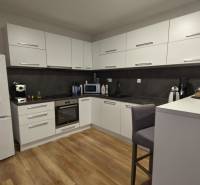 2-izbový byt na predaj, Vráble – sídl. Lúky, 56 m2 - Kuchyňa v 2-izbovom byte s bielymi skrinkami a podlahou s dreveným dekorom.