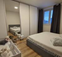 2-izbový byt na predaj, Vráble – sídl. Lúky, 56 m2 - Spálňa v 2-izbovom byte s podlahou s dreveným dekorom, posteľou a detskou postieľkou.