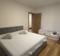 2-izbový byt na predaj, Vráble – sídl. Lúky, 56 m2 - Spálňa so sivou posteľou a detskou postieľkou, podlaha s dreveným dekorom v 2-izbovom byte.