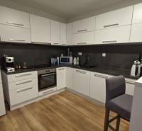 2-izbový byt na predaj, Vráble – sídl. Lúky, 56 m2 - Kuchyňa v 2-izbovom byte s podlahou s dreveným dekorom a bielymi skrinkami.
