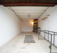 TOP LOKALITA - Garáž na predaj - Trenčín - Priestranný interiér Garáže s kovovými policami a bielymi stenami.