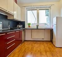 2-IZB. BYT, ČIASTOČNE ZARIADENÝ, TERASA , MOSTI PRI BRATISLAVE  - Kuchyňa v 2-izbovom byte s červenými skrinkami a podlahou s dreveným dekorom.