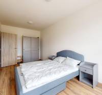 | 3-izbový byt v novostavbe, ul. Odevná + parking | Trenčín  - Spálňa v 3-izbovom byte s podlahou s dreveným dekorom, sivou posteľou a šatníkom.