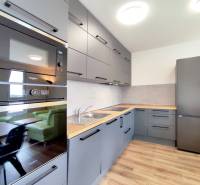 | 3-izbový byt v novostavbe, ul. Odevná + parking | Trenčín  - Kuchyňa v 3-izbovom byte s podlahou s dreveným dekorom, šedé skrinky, vstavané spotrebiče.