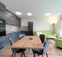 | 3-izbový byt v novostavbe, ul. Odevná + parking | Trenčín  - Svetlá kuchyňa s jedálenským stolom a pohovkou v 3-izbovom byte s podlahou s dreveným dekorom.