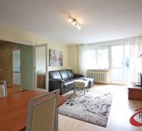 **PREDAJ 3-IZBOVÉHO BYTU S BALKÓNOM A LOGGIOU PRI SLUBEKOVEJ ZÁHRADE** - Obývačka v 3-izbovom byte s podlahou s dreveným dekorom a čiernou pohovkou.