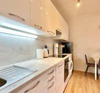 – PRENAJOM – 2 IZBOVÝ BYT 52 m² – OSTREDKOVA – RUŽINOV  - Kuchyňa v 2-izbovom byte s podlahou s dreveným dekorom, jedálenským stolom a spotrebičmi.
