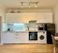 – PRENAJOM – 2 IZBOVÝ BYT 52 m² – OSTREDKOVA – RUŽINOV  - Kuchyňa v 2-izbovom byte s bielymi skrinkami a podlahou s dreveným dekorom.