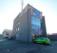 Predaj modernej administratívnej budovy v Bratislave, okres II - Budova so sklenou fasádou, parkoviskom a zelenej auto. Nachádza sa v priemyselnej oblasti.