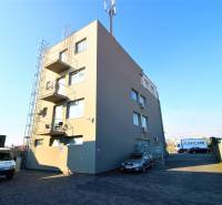 Predaj modernej administratívnej budovy v Bratislave, okres II - Budova na snímke s parkoviskom a zaparkovanými autami na pozemku.