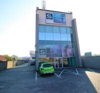 Predaj modernej administratívnej budovy v Bratislave, okres II - Štvorposchodová budova so sklenenou fasádou a parkoviskom pred vchodom.