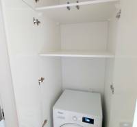 JEDINEČNÝ 2i byt, NOVOSTAVBA, KLÍMA, VÝHĽAD, PARKING, SKY PARK - Práčka zabudovaná v bielom skrini v 2-izbovom byte, úložné police nad ňou.