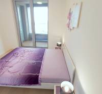 JEDINEČNÝ 2i byt, NOVOSTAVBA, KLÍMA, VÝHĽAD, PARKING, SKY PARK - Posteľ s fialovým povlečením, stolík a lampa v 2-izbovom byte.