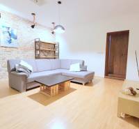 JEDINEČNÝ 2i byt, REKONŠT., 2 X .SAMOST.IZBA, Hviezdoslavovo nám.  - Obývacia izba na ulici Hviezdoslavovo námestie, 2-izbový byt s tehlovou stenou a šedou sedačkou.