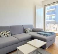 MODERNÝ 3i byt, CUBICON GARDENS, BALKÓN, PARKING, Rudolfa Mocka - Obývacia izba v 3-izbovom byte s pohovkou a balkónom, podlaha s dreveným dekorom.