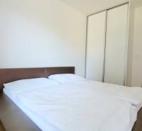 MODERNÝ 3i byt, CUBICON GARDENS, BALKÓN, PARKING, Rudolfa Mocka - Spálňa v 3-izbovom byte s veľkou posteľou, skriňou a podlahou s dreveným dekorom.